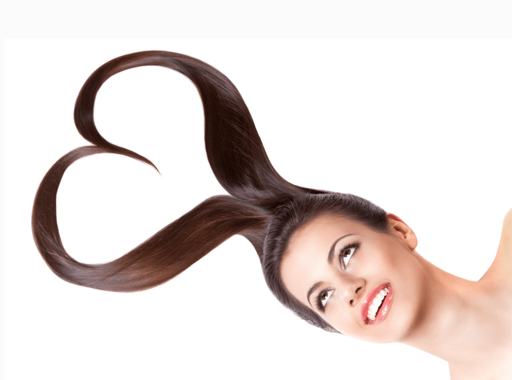 A woman with long, glossy hair styled into a heart shape, smiling joyfully against a white background. Highlights playful hair creativity.