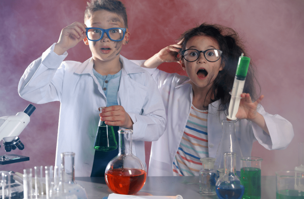 Two excited children in lab coats react with surprise during a science experiment, surrounded by colorful beakers and a microscope.